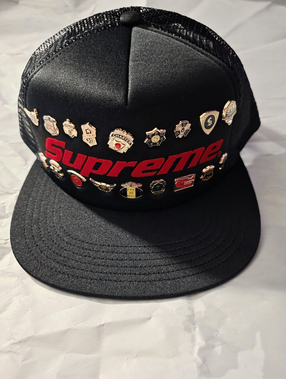 Supreme Trucker Black Cap with Red Logo and Gold Pins.